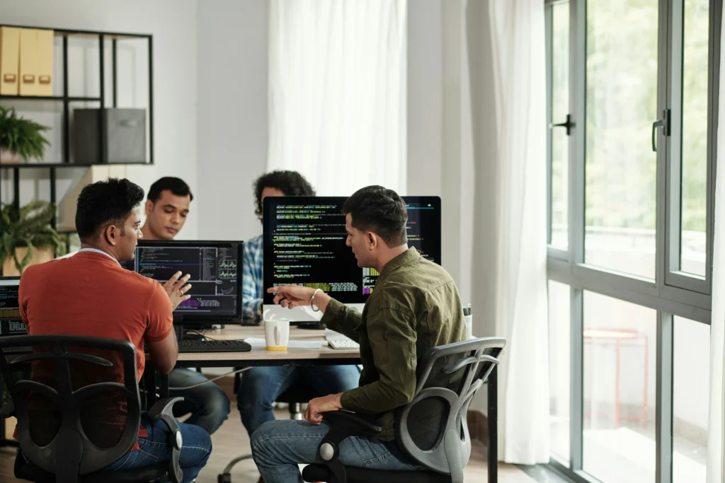 Group of Topshelf Technology Denver developers discussing and reviewing code on computer monitors in a shared office.