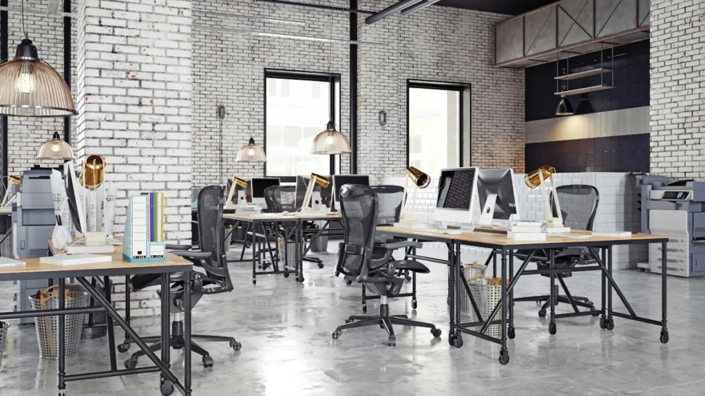 Modern Industrial Office Workspace With White Brick Walls, Wooden Desks, Mesh Office Chairs, Desktop Computers, Pendant Lighting, And Polished Concrete Floors.