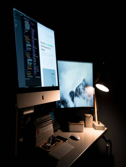 Two mac monitors in low dark light, one had code on it and the other has snowing mountain caps.