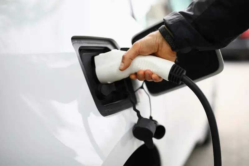 Hand plugging a charging cable into a white electric vehicle