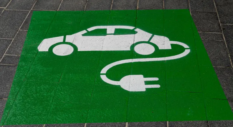 Painted symbol of an electric car with a charging cable on green pavement and solid-state batteries tesla