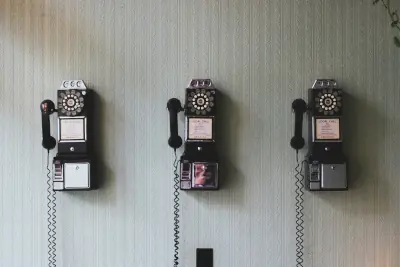 Three vintage rotary payphones mounted on a wall with handsets hanging