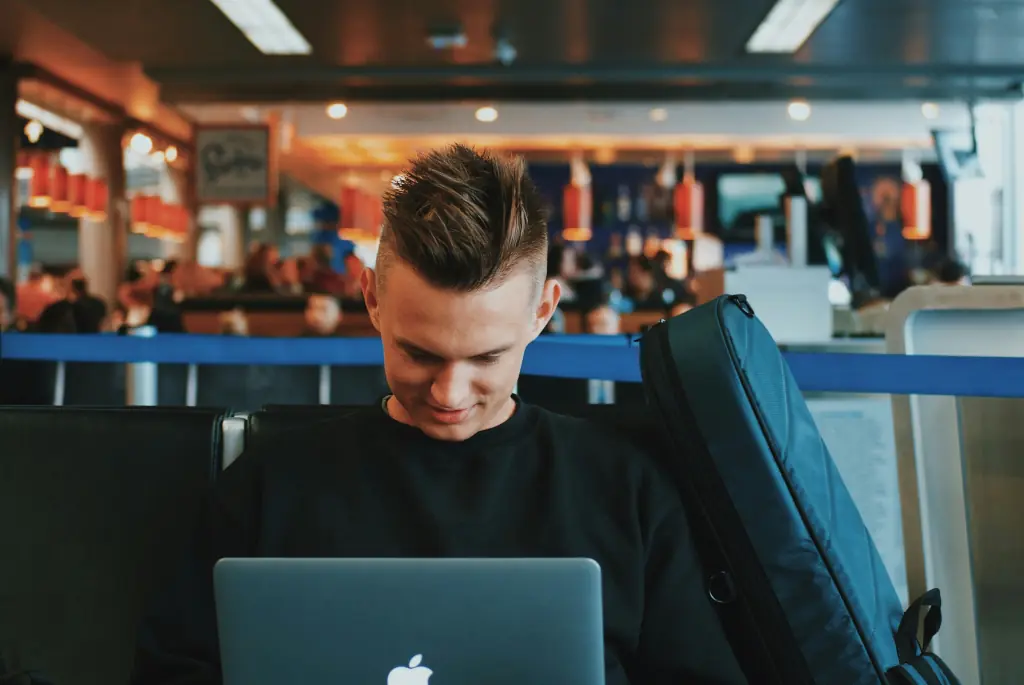 Man using a laptop in an airport terminal, possibly connected to public Wi-Fi
