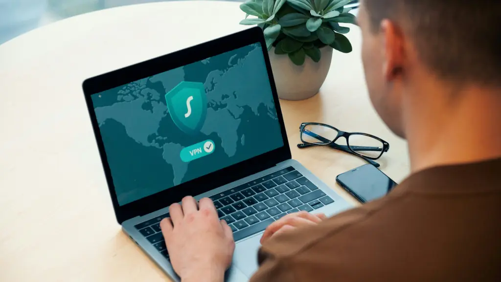 Man using a VPN on a MacBook laptop with a world map and security shield on screen