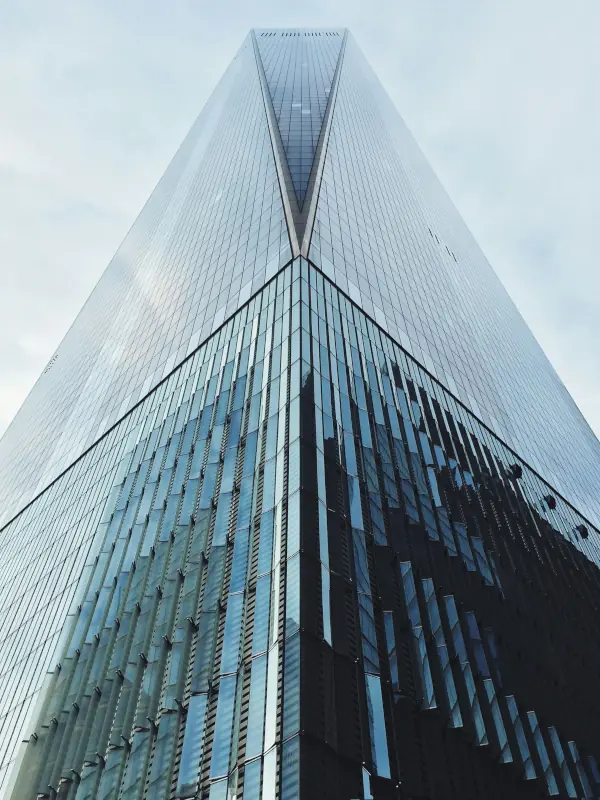 Upward view of a modern glass skyscraper against a cloudy sky